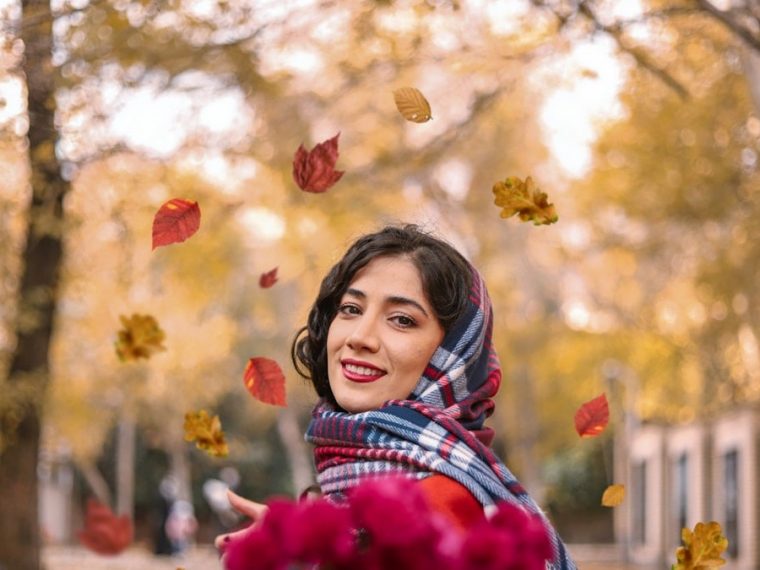 girl in red and white plaid scarf standing under red flowers